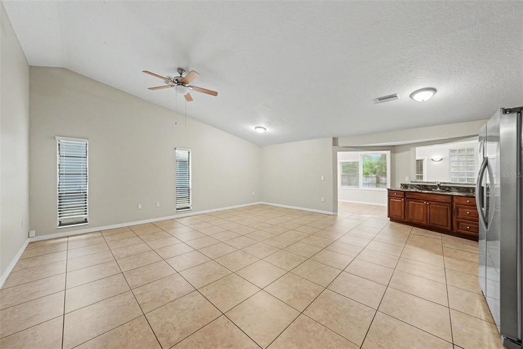 A spacious living area with vaulted ceilings, tile flooring, and an adjacent kitchen counter area — 7623 BRAMBLEWOOD DRIVE, PORT RICHEY, FL