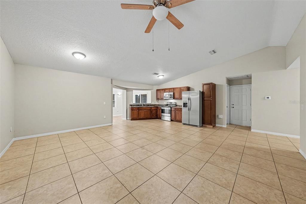 An open-concept kitchen and living area features tile flooring, wood cabinets, and stainless steel appliances — 7623 BRAMBLEWOOD DRIVE, PORT RICHEY, FL