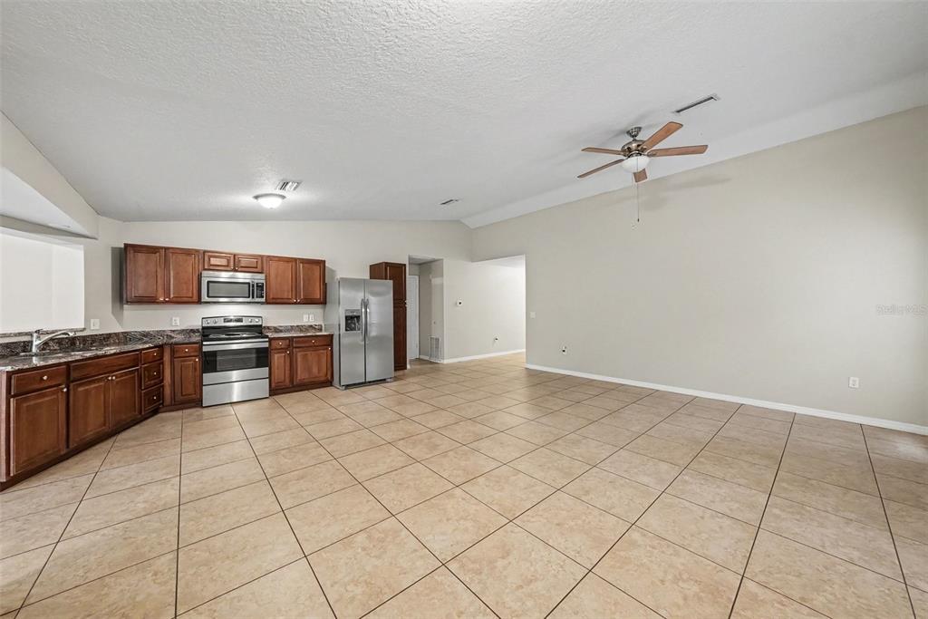 A kitchen with wood cabinets, stainless steel appliances, and tile flooring opens to a living area — 7623 BRAMBLEWOOD DRIVE, PORT RICHEY, FL