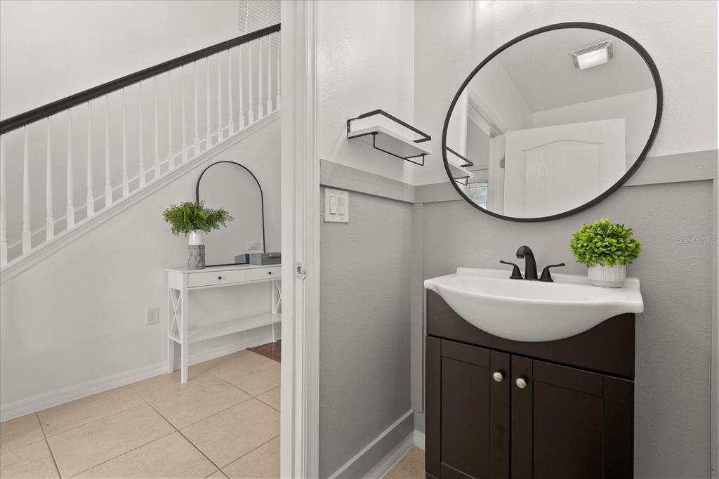 A small bathroom features a dark vanity, round mirror, and gray wainscoting next to stairs — 3597 UMBRELLA COURT, TAVARES, FL