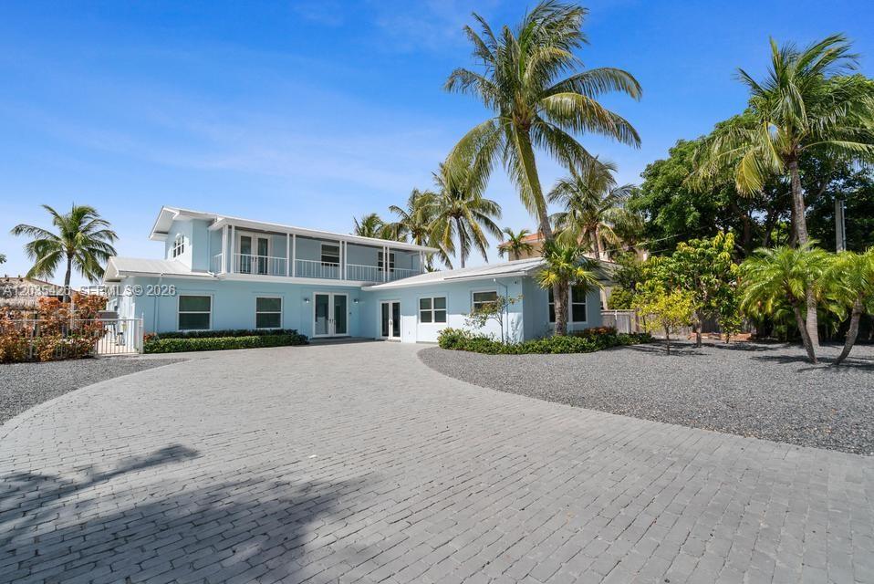 A two-story light blue house features a paved driveway and several palm trees — DUCK, FL