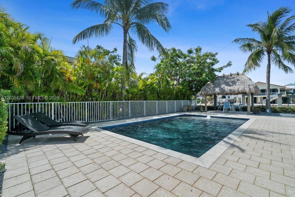 A rectangular swimming pool sits on a paved patio next to lounge chairs and a tiki — DUCK, FL