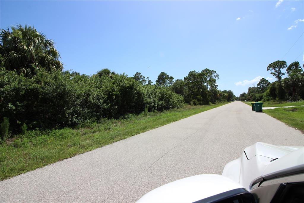 A paved road runs alongside a dense, wooded lot under a clear blue sky — 26351 BROOKS ROAD, PUNTA GORDA, FL