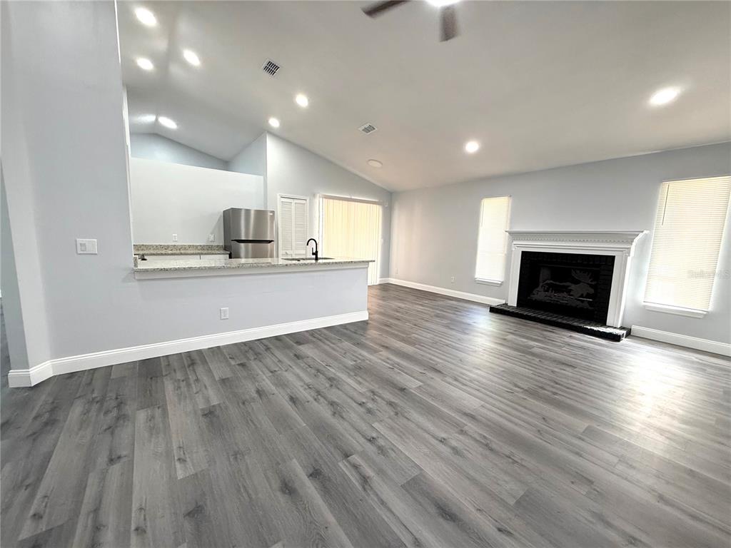 An open-concept living room features gray wood-look flooring, a fireplace, and a kitchen island — 2419 LIELA LEE COURT, OCOEE, FL