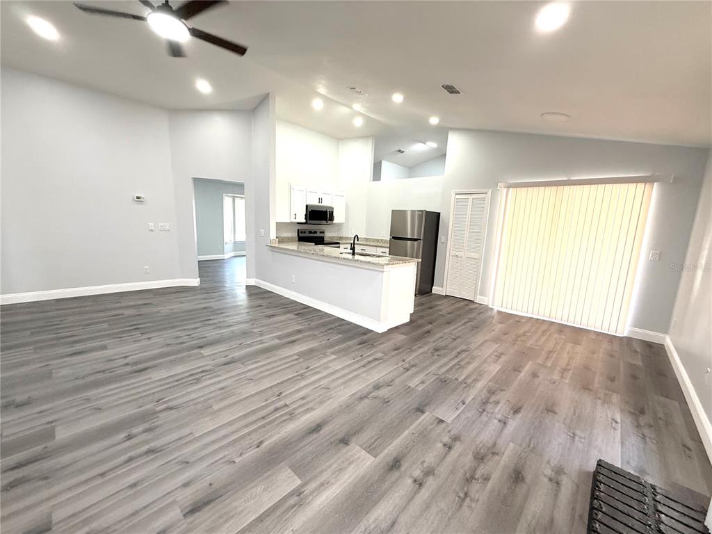 An open-concept living area features gray wood-look flooring, a kitchen with white cabinets, and sliding glass doors — 2419 LIELA LEE COURT, OCOEE, FL