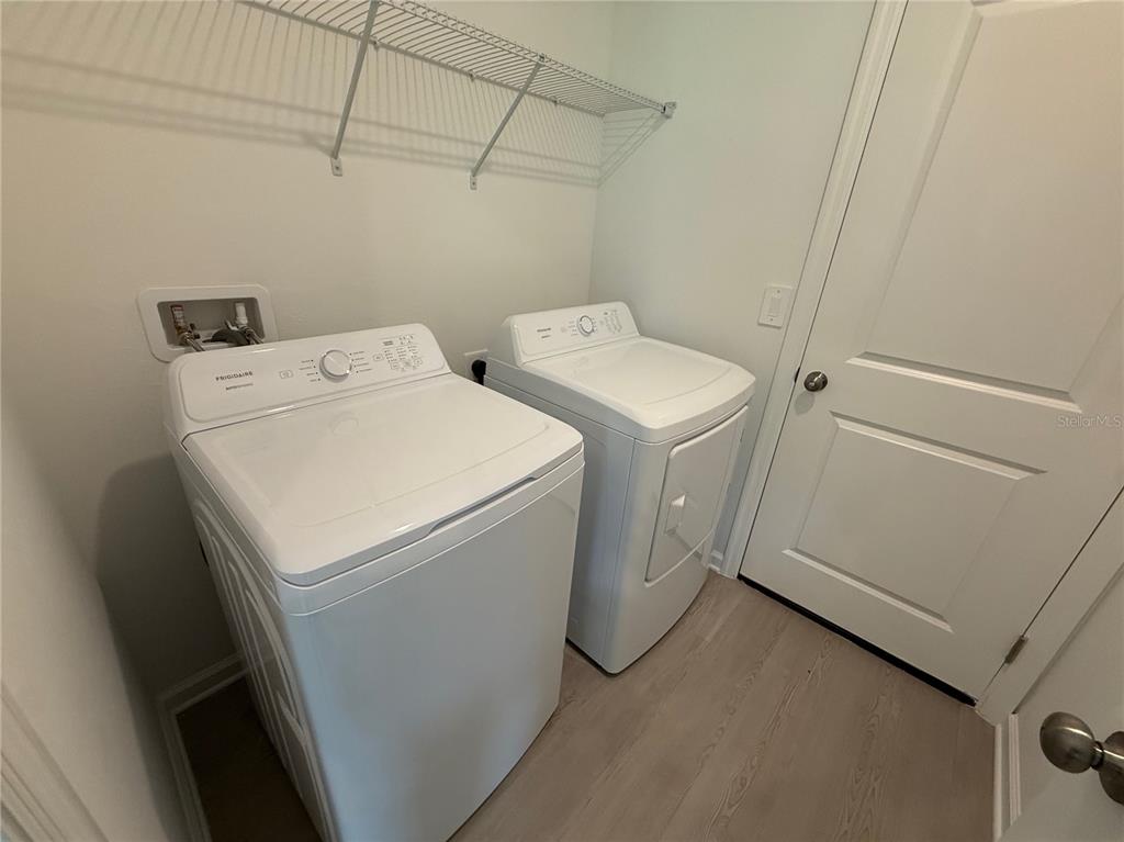 A laundry room features a white washer and dryer set beneath a wire storage shelf — 6224 BOTTICELLA BOULEVARD, WINTER HAVEN, FL