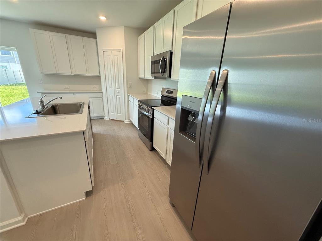 A modern kitchen features white cabinets, stainless steel appliances, and light wood-look flooring — 6224 BOTTICELLA BOULEVARD, WINTER HAVEN, FL