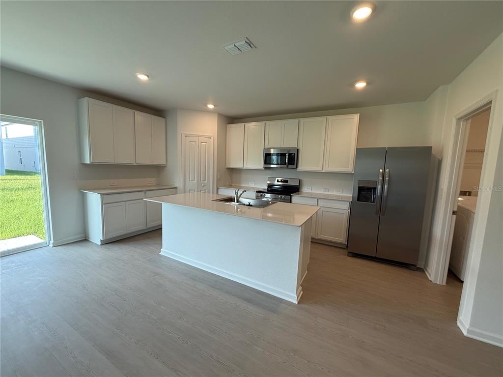 A kitchen with white cabinets, stainless steel appliances, a center island, and light wood flooring — 6224 BOTTICELLA BOULEVARD, WINTER HAVEN, FL