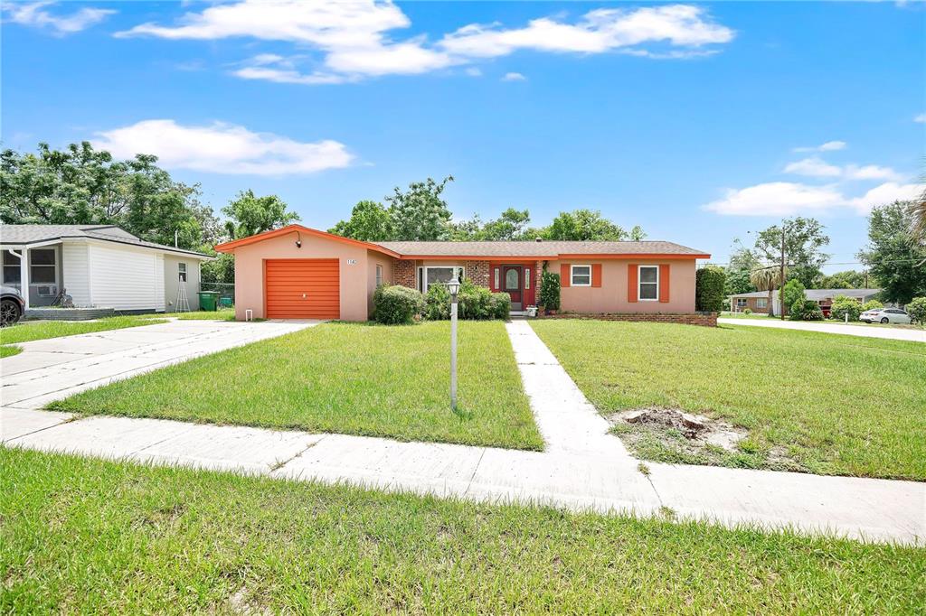 A single-story house with a tan exterior, orange garage door, and a front lawn — 1140 COBBLESTONE AVENUE, DELTONA, FL