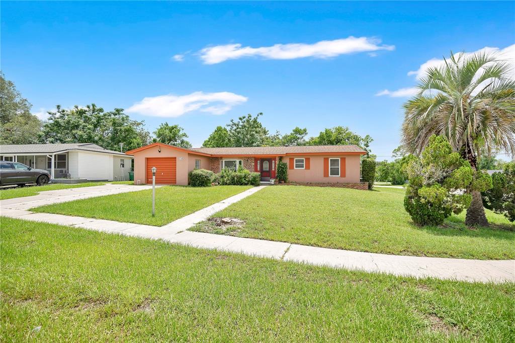 A single-story house with a tan exterior, orange garage door, and a front lawn — 1140 COBBLESTONE AVENUE, DELTONA, FL