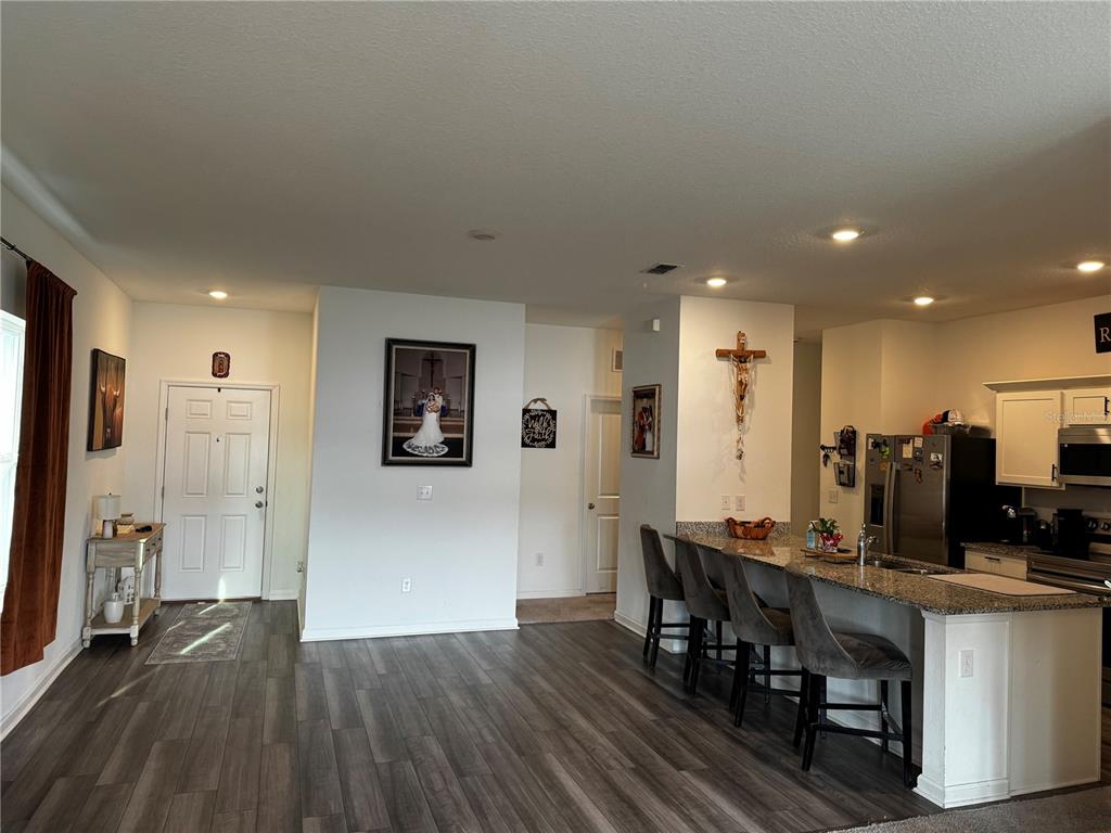 An open-concept kitchen with a granite breakfast bar overlooks a living area with wood-look flooring — 927 KELLY FERN LOOP, RUSKIN, FL