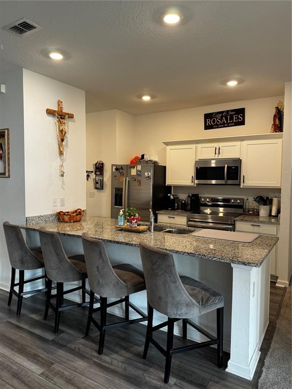 A kitchen features white cabinets, granite countertops, a breakfast bar with four gray stools, and stainless steel appliances — 927 KELLY FERN LOOP, RUSKIN, FL