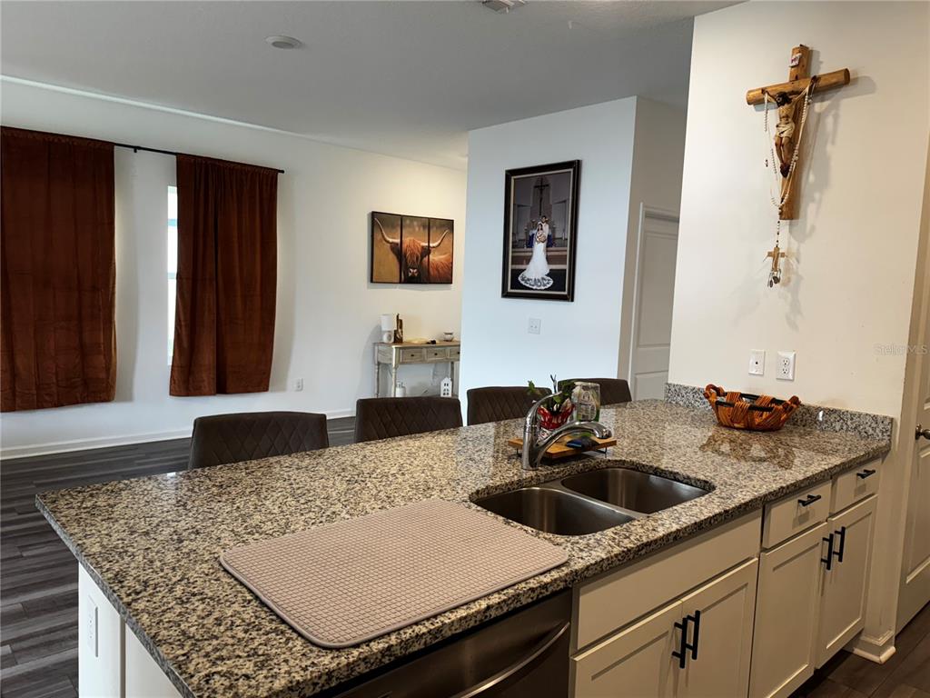 A kitchen island with a granite countertop and stainless steel sink faces a dining area — 927 KELLY FERN LOOP, RUSKIN, FL