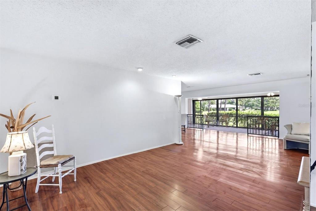A living room with hardwood floors, white walls, and a large window overlooking a balcony — 5451 GOLF POINTE DRIVE UNIT V-225, SARASOTA, FL