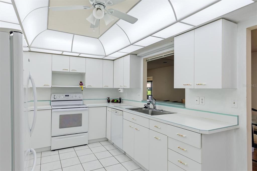 A white kitchen features a tray ceiling, tiled floors, and a pass-through window — 5451 GOLF POINTE DRIVE UNIT V-225, SARASOTA, FL
