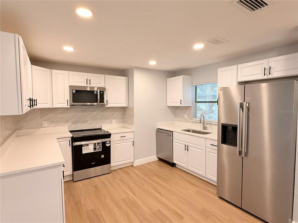 A kitchen features white cabinets, stainless steel appliances, light countertops, and wood-look flooring — 1790 WILLIAMS MANOR AVENUE, ORLANDO, FL