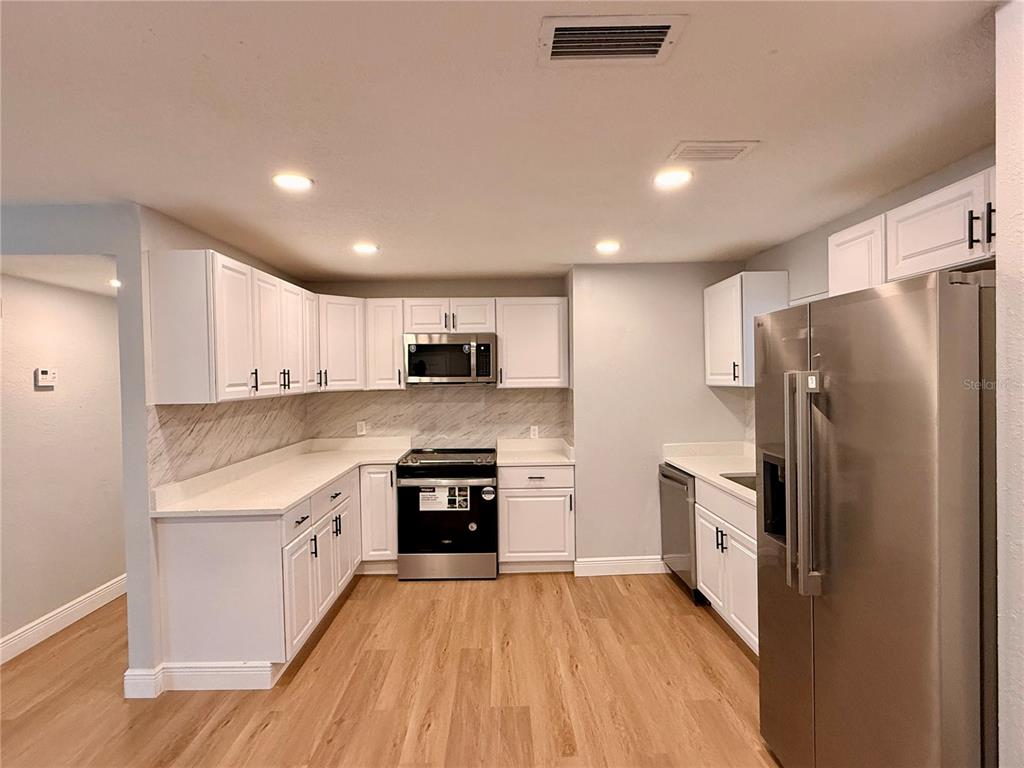 A kitchen features white cabinets, stainless steel appliances, light countertops, and wood-look flooring — 1790 WILLIAMS MANOR AVENUE, ORLANDO, FL