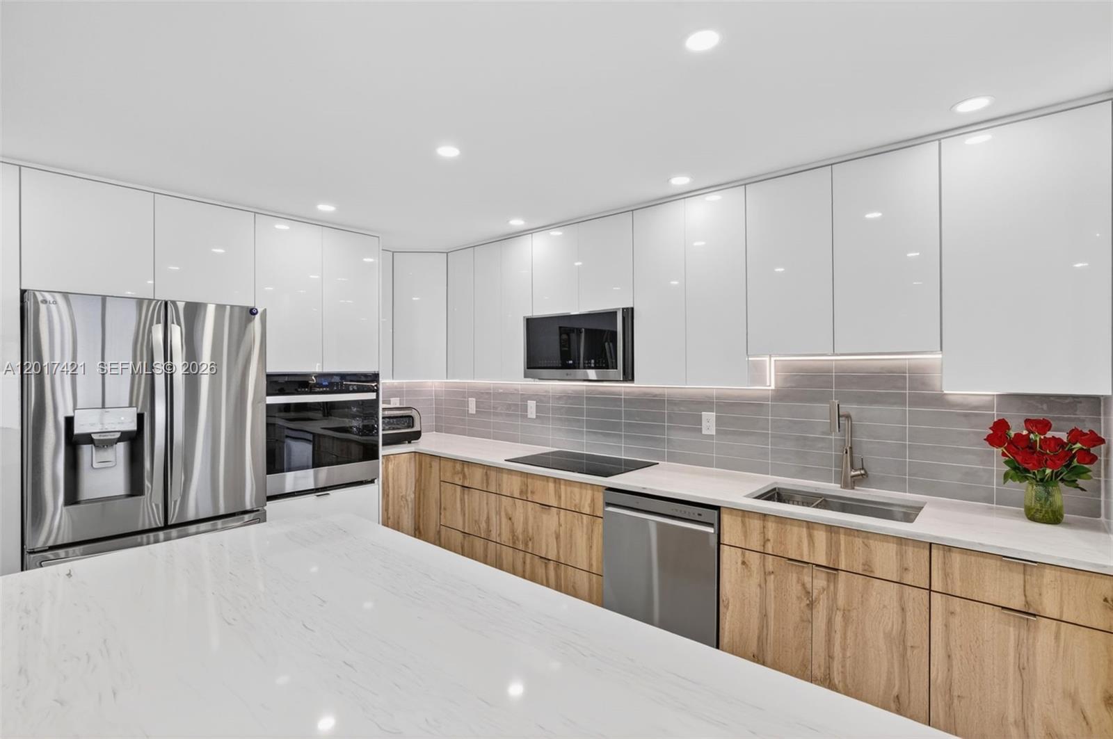 A modern kitchen features white upper cabinets, wood-grain lower cabinets, and a white marble island — 3848 Atlanta St, Hollywood FL 33021, HOLLYWOOD, FL