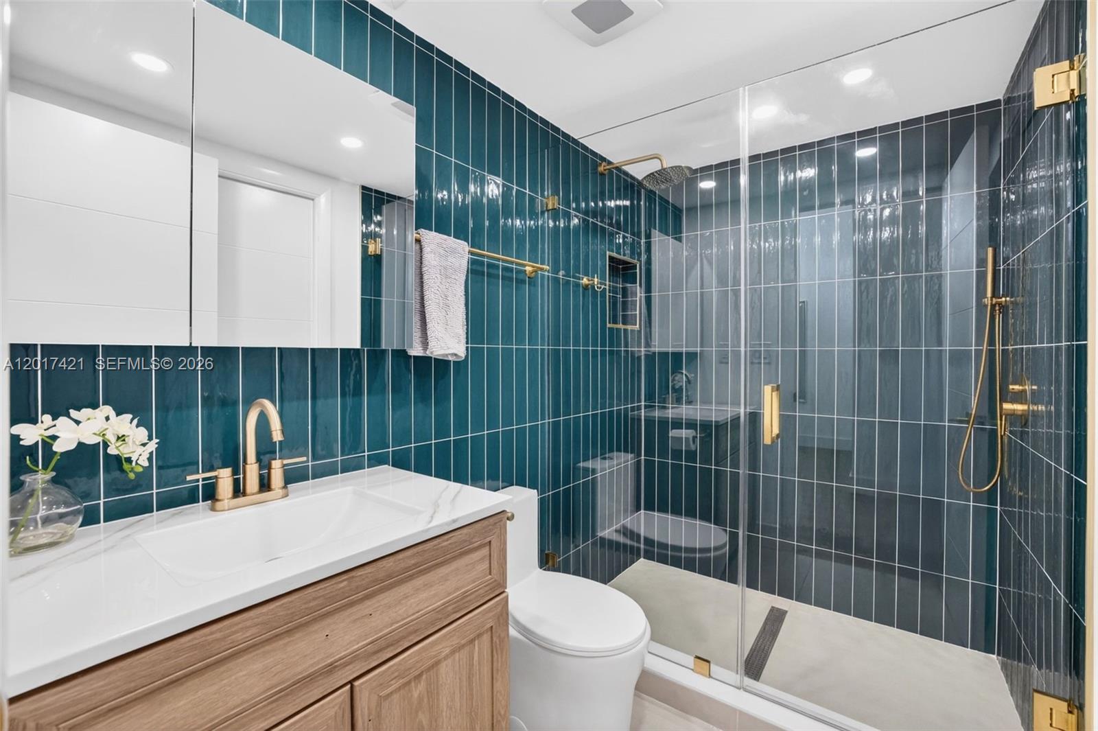 A bathroom features teal vertical subway tiles, a wood vanity, and a glass-enclosed shower — 3848 Atlanta St, Hollywood FL 33021, HOLLYWOOD, FL