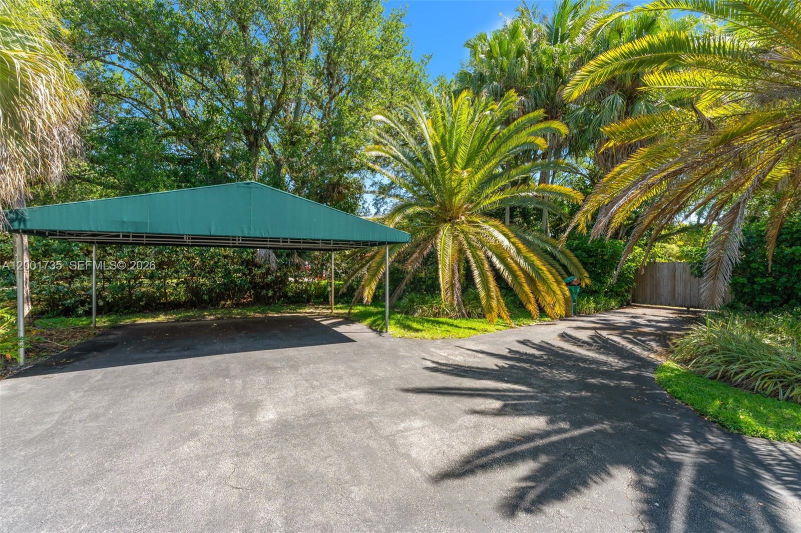 A green metal carport stands on an asphalt driveway surrounded by palm trees and foliage — 11401 SW 102nd Ave, Miami FL 33176, MIAMI, FL
