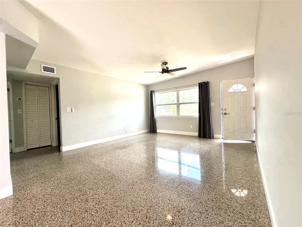 An empty living room features light gray walls, a ceiling fan, and speckled epoxy flooring — 126 11TH AVENUE SW, LARGO, FL