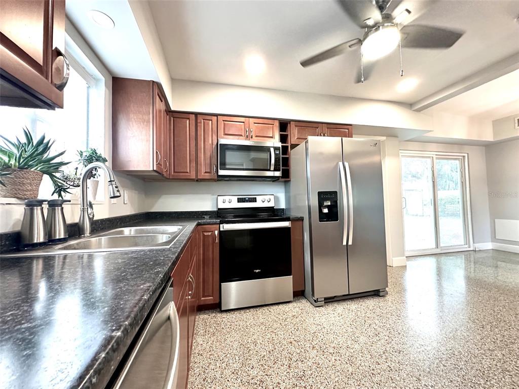 A kitchen features wood cabinets, stainless steel appliances, dark countertops, and a speckled floor — 126 11TH AVENUE SW, LARGO, FL