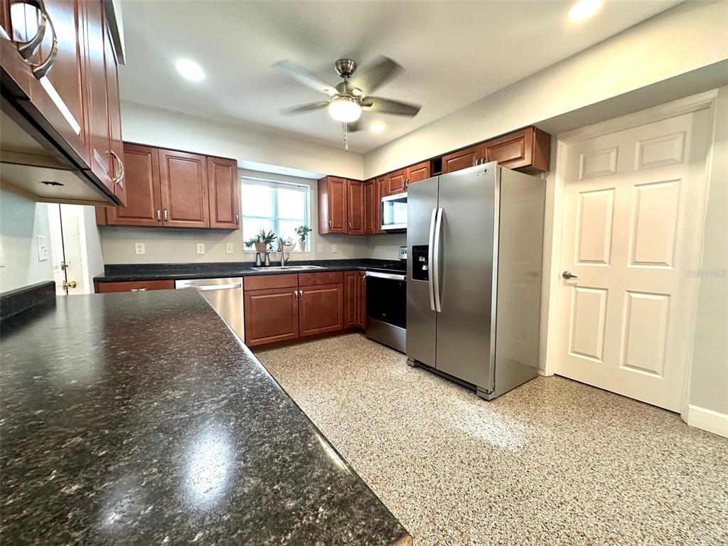A kitchen features dark wood cabinets, black countertops, stainless steel appliances, and speckled flooring — 126 11TH AVENUE SW, LARGO, FL