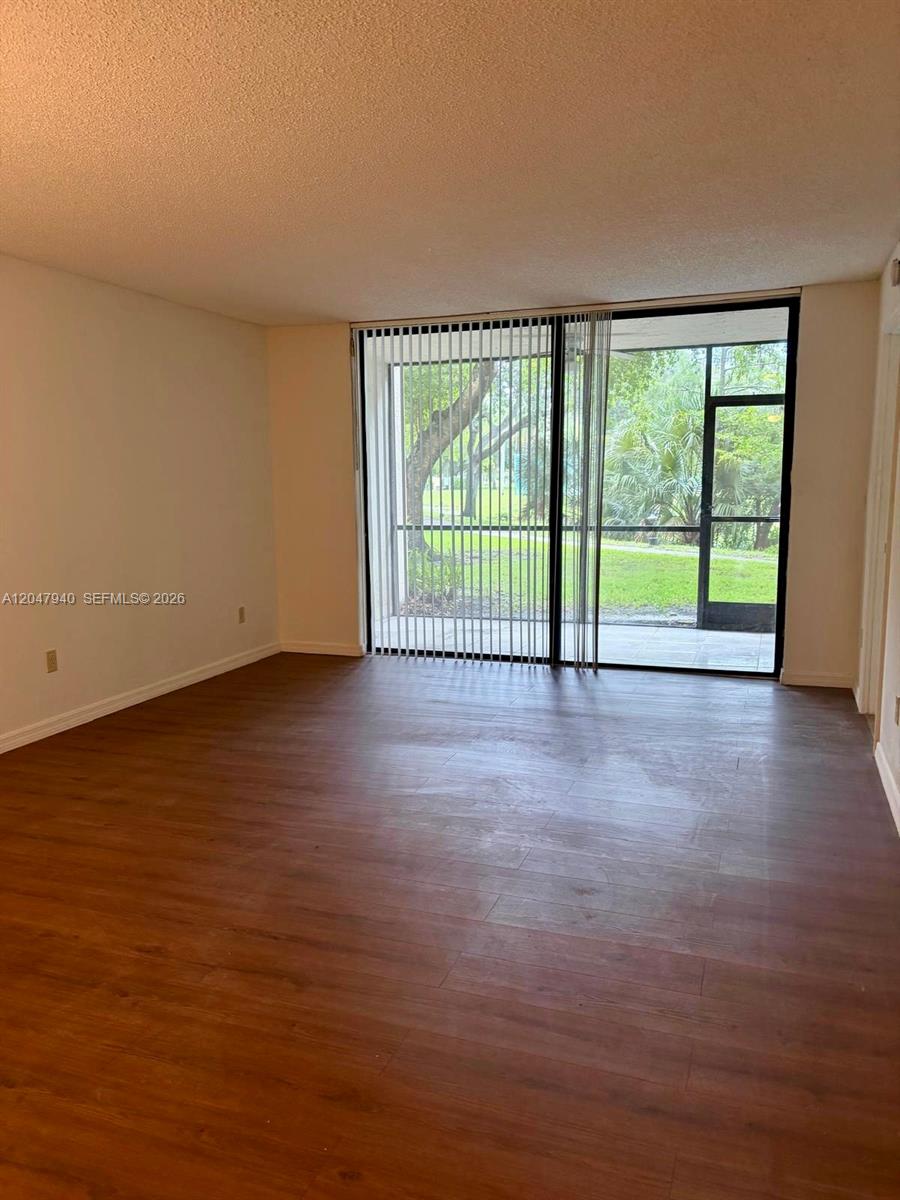 An empty room features wood-look flooring, plain walls, and a sliding glass door to a patio — 100 NW 76th Ave # 2, Plantation FL 33324, PLANTATION, FL
