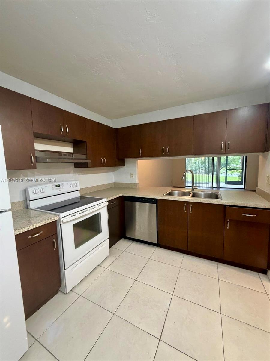 A kitchen features dark wood cabinets, white appliances, a double sink, and light tile flooring — 100 NW 76th Ave # 2, Plantation FL 33324, PLANTATION, FL