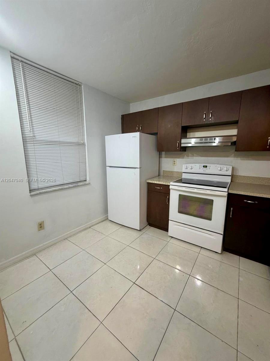 A kitchen features white appliances, dark wood cabinets, and light-colored tile flooring — 100 NW 76th Ave # 2, Plantation FL 33324, PLANTATION, FL