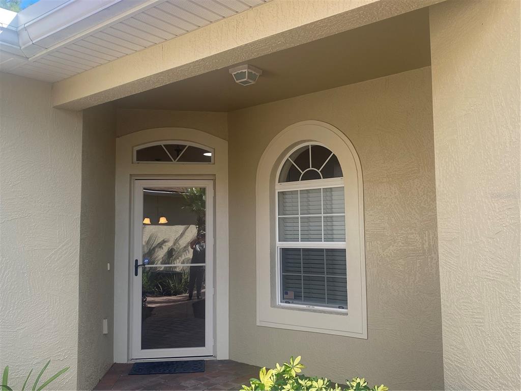 A beige stucco home entrance features a glass storm door and an arched window — 1561 VIENNA SQUARE DRIVE, WINTER HAVEN, FL