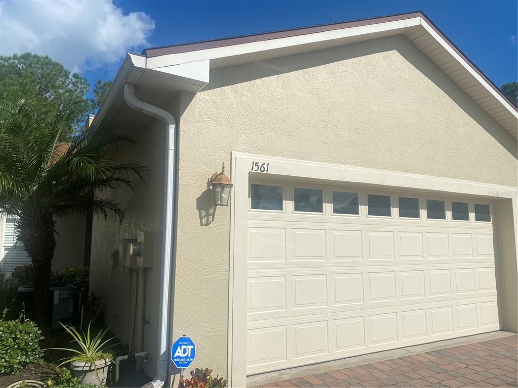 A beige house exterior features a two-car garage, a palm tree, and an ADT sign — 1561 VIENNA SQUARE DRIVE, WINTER HAVEN, FL