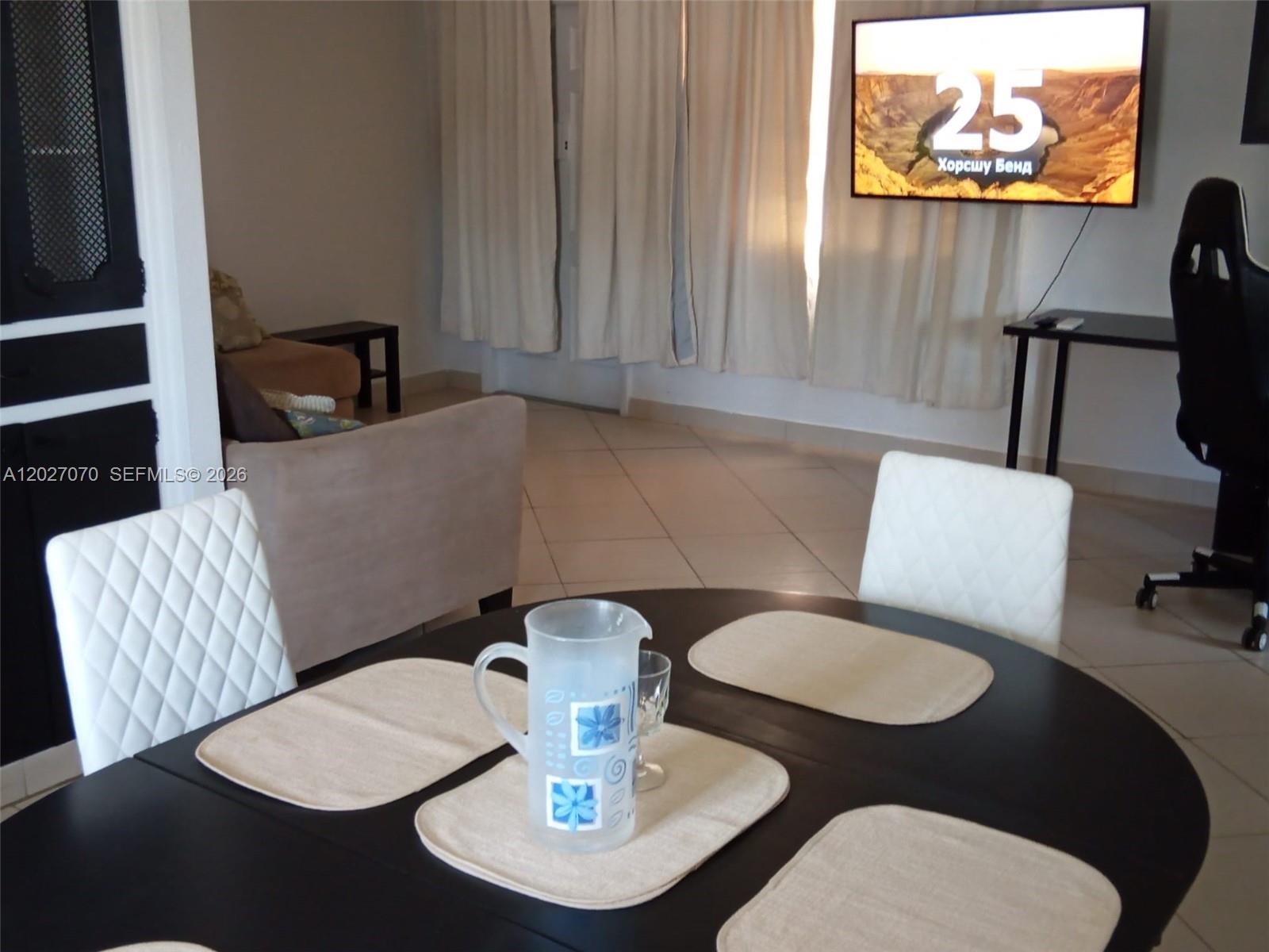 A dining area with a dark round table and white chairs faces a living room — 1110 N 16 Ave # 1, Hollywood FL 33020, HOLLYWOOD, FL