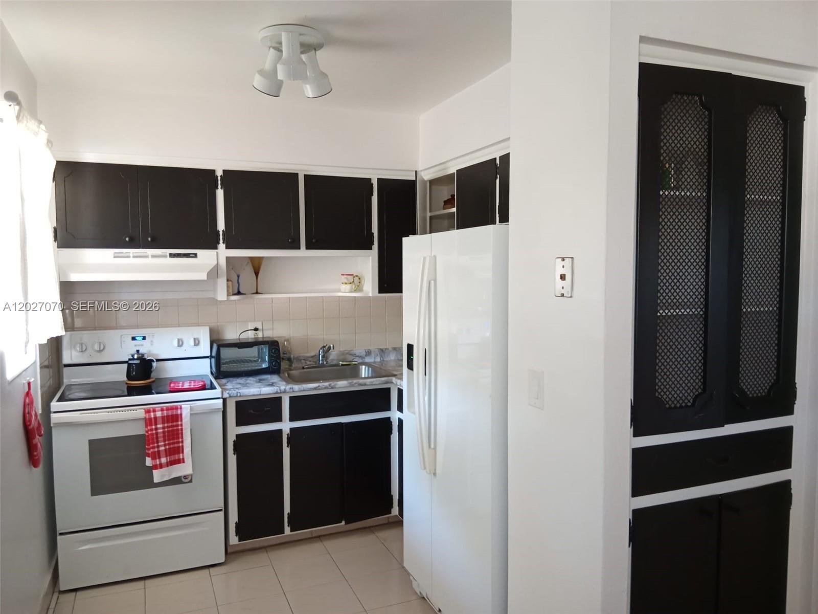 A kitchen features white appliances, black cabinets, and a tall pantry with mesh door panels — 1110 N 16 Ave # 1, Hollywood FL 33020, HOLLYWOOD, FL