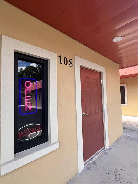 The exterior of a commercial building features a red door, a window with a neon sign, and the number 108 — 5207 26TH STREET W, BRADENTON, FL