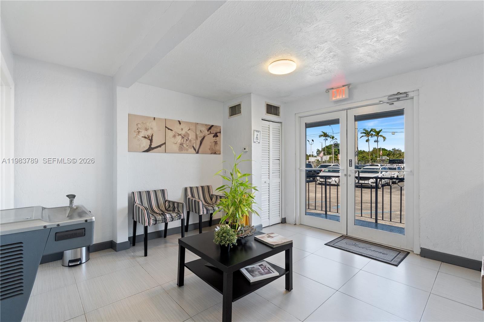 A waiting area features two striped chairs, a coffee table, a plant, and glass doors — 8800 NW 27th Ave # A, Miami FL 33147, MIAMI, FL