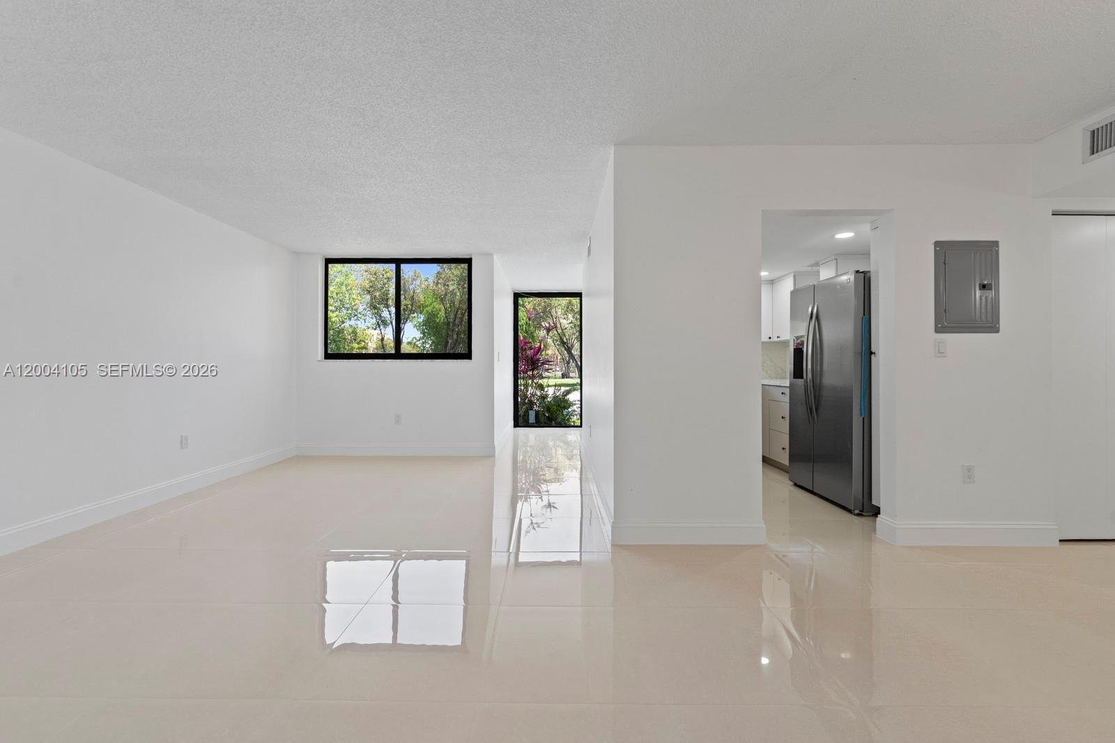A bright, empty living room with white walls, glossy tile floors, and an adjacent kitchen — 9440 W Flagler St # 106, Miami FL 33174, MIAMI, FL
