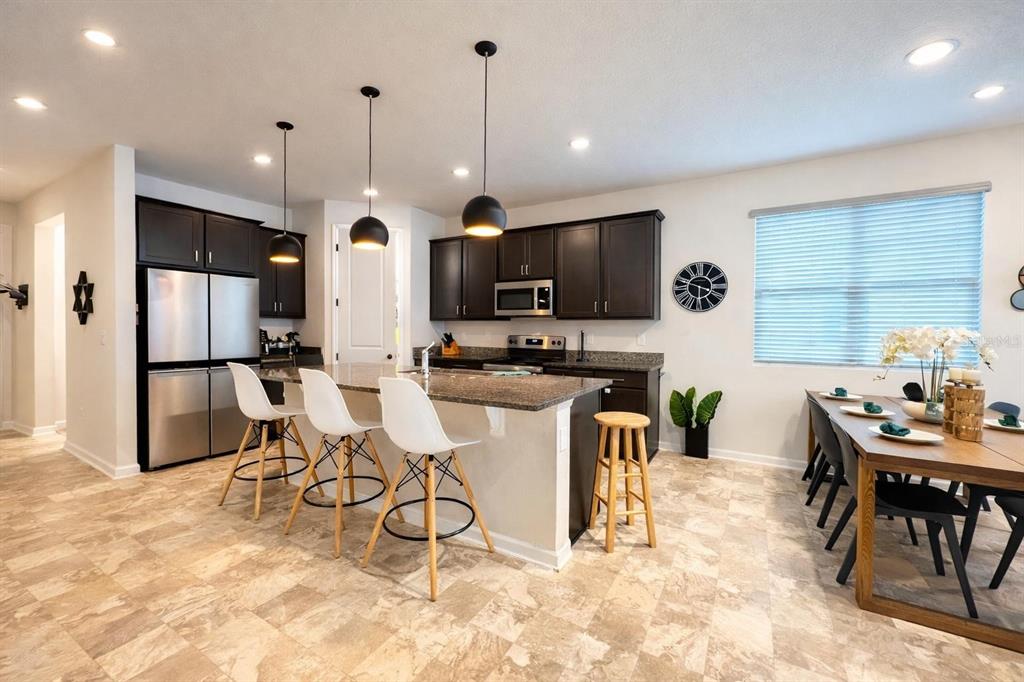 A kitchen features dark cabinets, granite countertops, a breakfast bar with stools, and dining area — 1220 MATTIE POINTE BOULEVARD, AUBURNDALE, FL