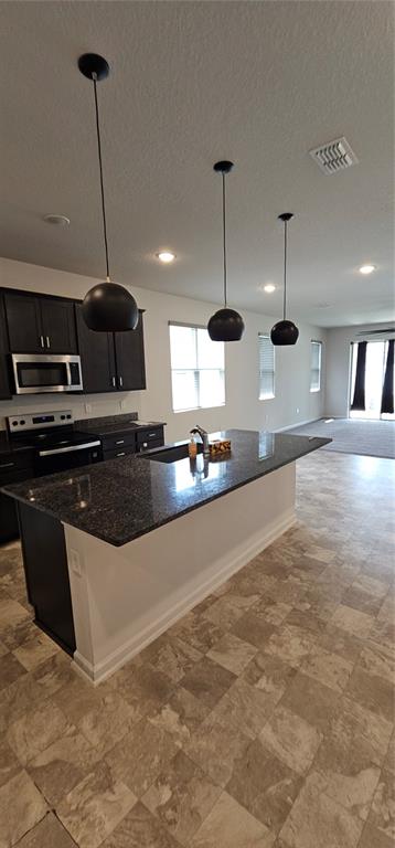 A kitchen features a dark granite island, dark cabinetry, and three black pendant lights — 1220 MATTIE POINTE BOULEVARD, AUBURNDALE, FL