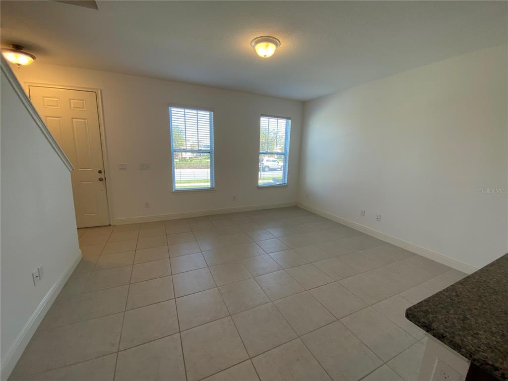 An empty room features light-colored tile flooring, two windows, and a white door — 15555 HONEYBELL DRIVE, WINTER GARDEN, FL