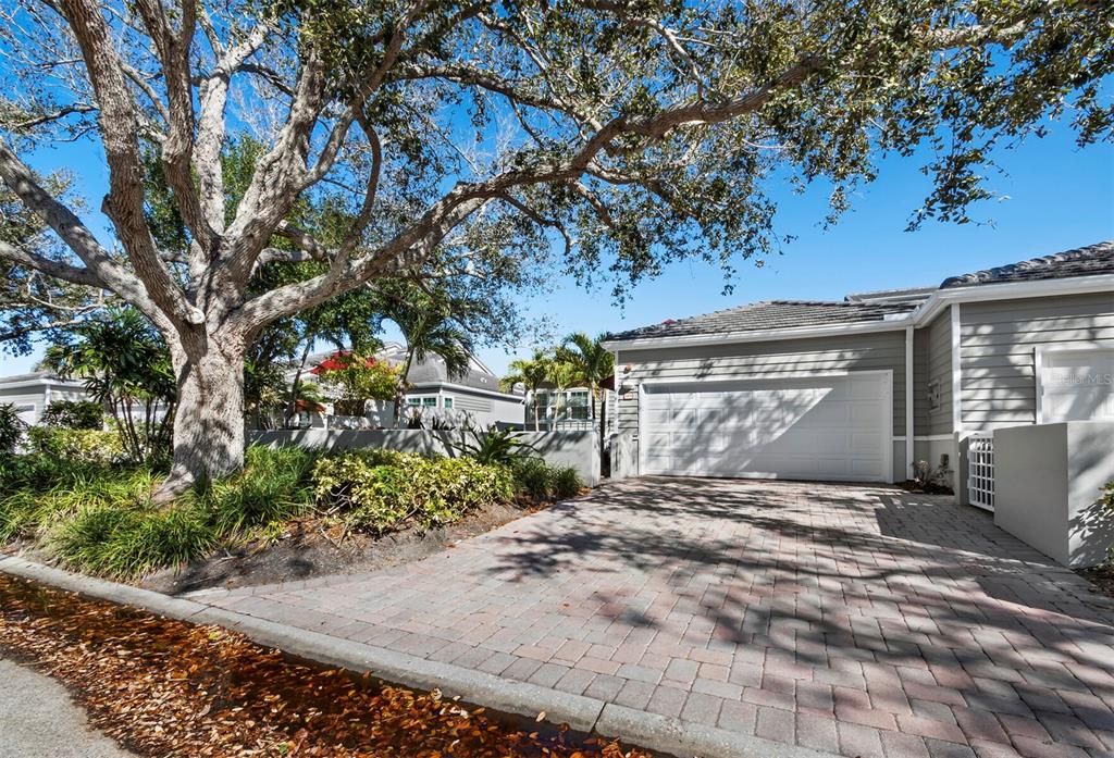A paved driveway leads to a gray house with a white garage door and large tree — 3435 WINDING OAKS DRIVE UNIT 18, LONGBOAT KEY, FL
