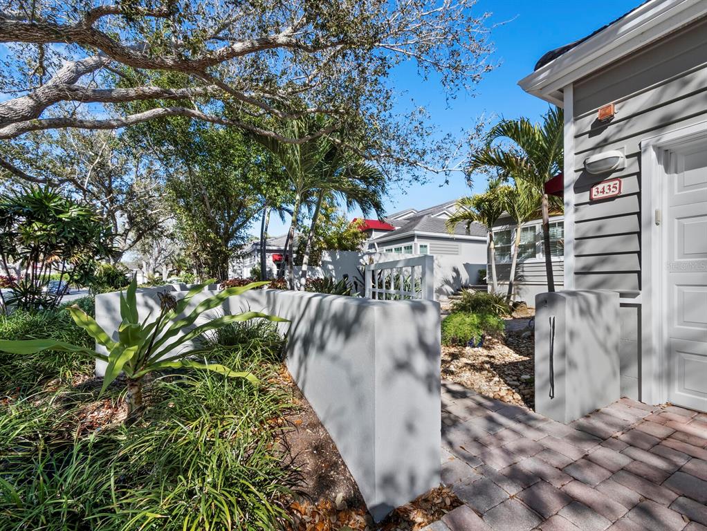 A paved walkway leads past a curved concrete wall toward the entrance of a house — 3435 WINDING OAKS DRIVE UNIT 18, LONGBOAT KEY, FL