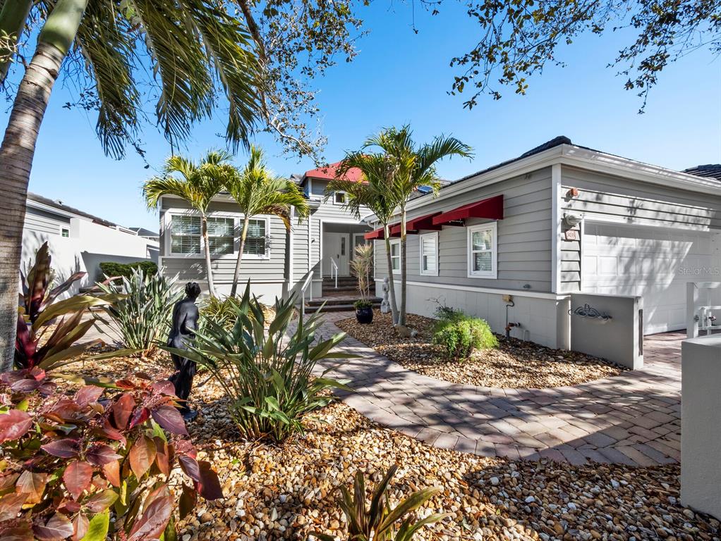 A single-story house with gray siding, red awnings, and a paved walkway through gravel landscaping — 3435 WINDING OAKS DRIVE UNIT 18, LONGBOAT KEY, FL