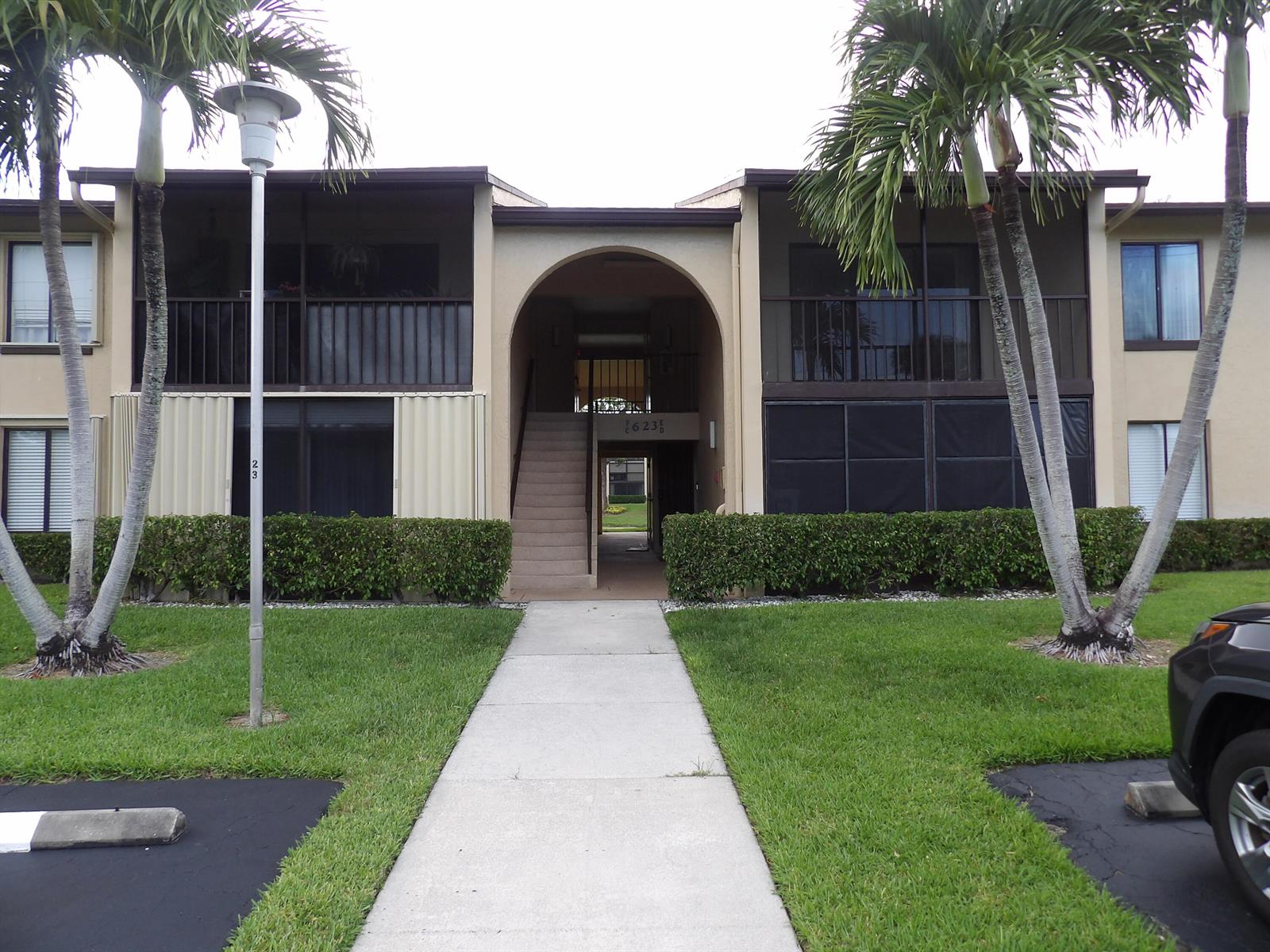 A two-story apartment building with a central arched entryway, palm trees, and a concrete walkway — 623 Sea Pine Way # D2, FL 33415, FL