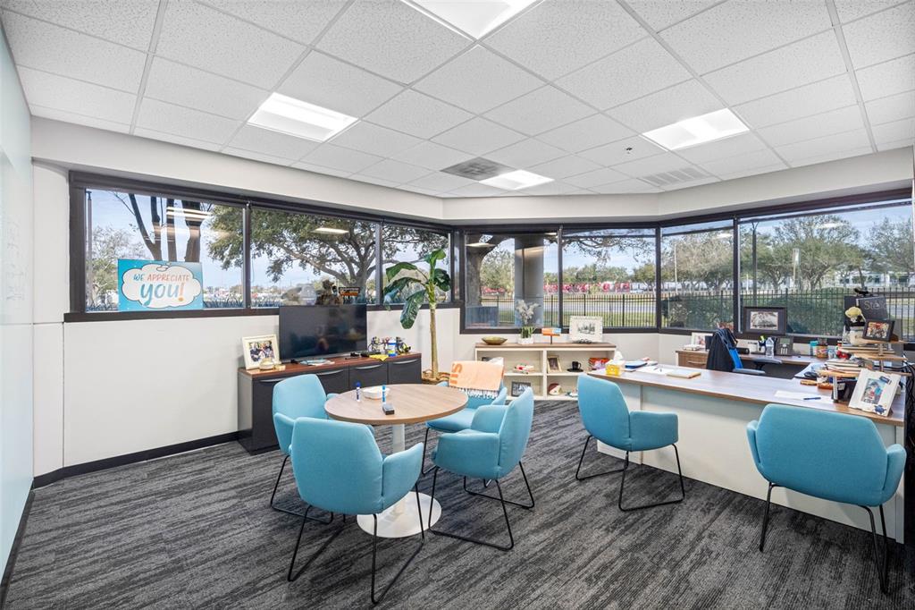 An office space features a round meeting table, blue chairs, a desk, and large windows — 6801 E HILLSBOROUGH AVENUE, TAMPA, FL