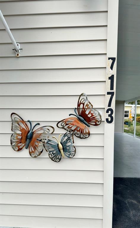 A vertical strip of house numbers 7173 is mounted on light-colored vinyl siding beside metal butterflies — 7173 MOUNT BRISTOL BOULEVARD NE UNIT 458, ST PETERSBURG, FL
