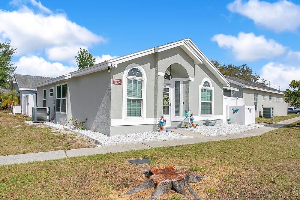 A single-story house with gray stucco siding, white trim, and a tree stump in front — 130 DEER SONG DRIVE, WINTER SPRINGS, FL