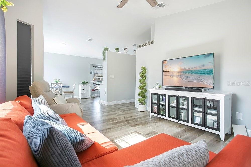 A living room features an orange sectional sofa, a television on a white cabinet, and wood-look flooring — 130 DEER SONG DRIVE, WINTER SPRINGS, FL