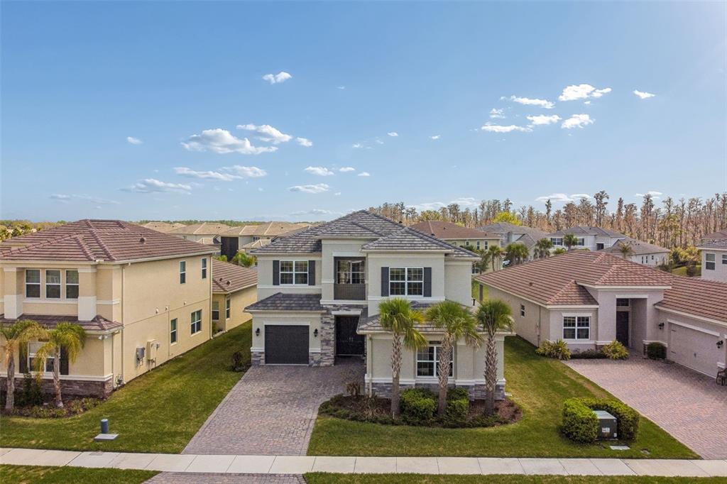 An aerial view shows a two-story suburban house with a tiled roof and paver driveway — 3416 ACACIA BAY AVENUE, WESLEY CHAPEL, FL