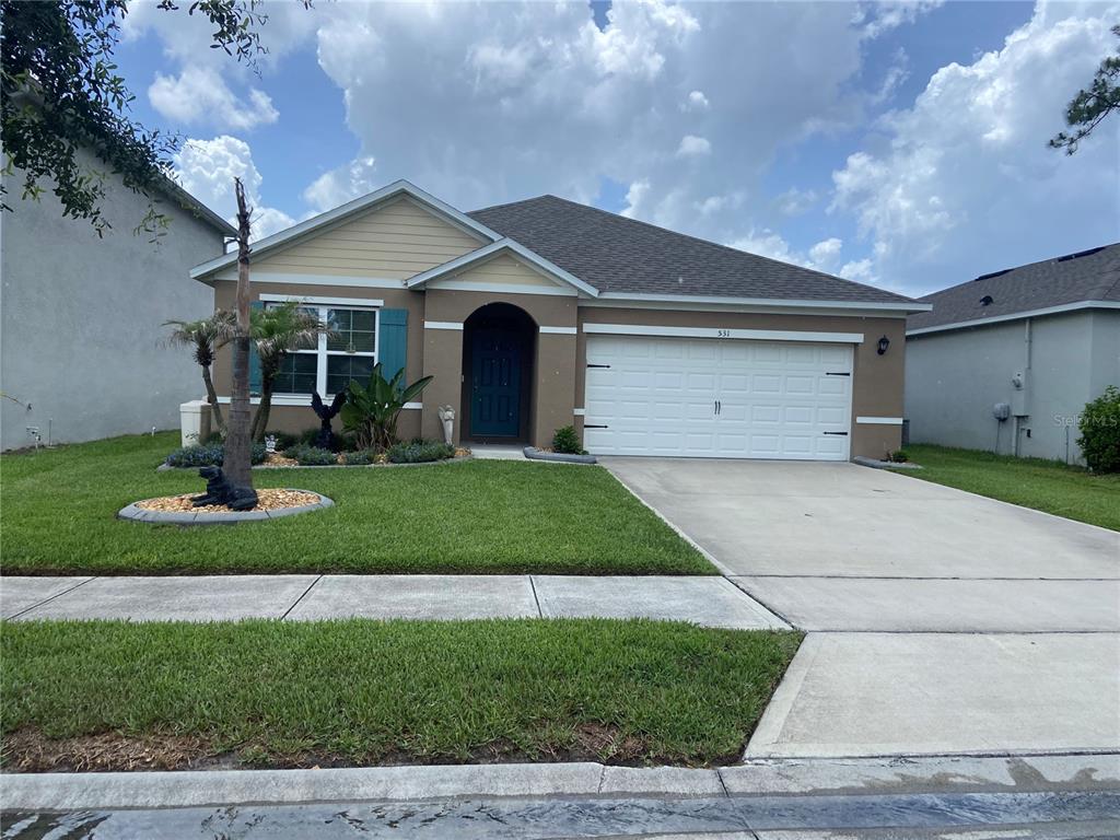A single-story house with a tan stucco exterior, a white garage door, and a front lawn — 531 EMILY GLEN STREET, DELAND, FL